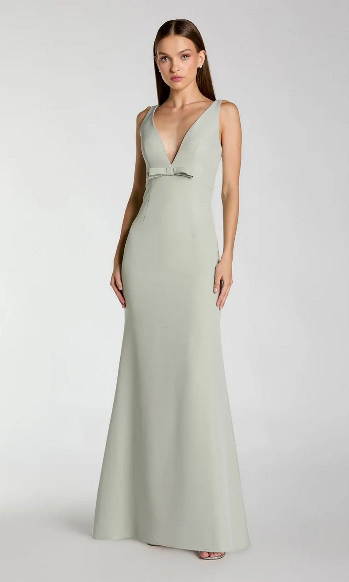 A woman wears the Mac Duggal 2371 long formal dress—a light gray, sleeveless fit-and-flare gown with a deep V-neckline, small waist bow, and elegant crepe fabric—standing against a plain background.
